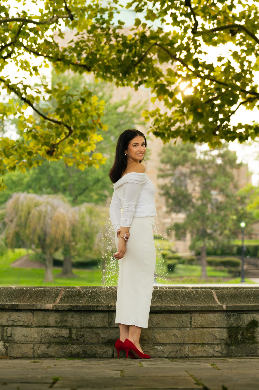 Woman in white outfit and red heels standing by a fountain